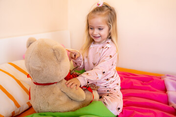 A happy little girl plays on the bed with her beloved teddy bear. The concept of childhood dreams...