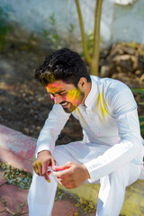 Portrait of handsome young man playing in the park on holi colours festival.