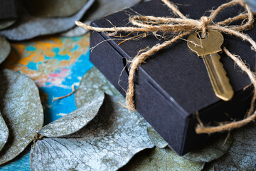 Black gift box close-up with a bronze vintage key decor on a nature leaves background
