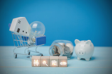 Icons people, magnifying glass, house, and money on wood blocks behind have a light bulb with a little wooden house on a blue shopping cart, and coins, white piggy bank on a blue desk. Loan Concept.