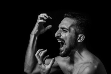 A man screams on a black background. Black and white male portrait. Expression of negative emotions