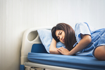 Obraz premium Asian woman patients, is sad and lying in patient's bed with alone, On white wall background, to people health care and health insurance concept.
