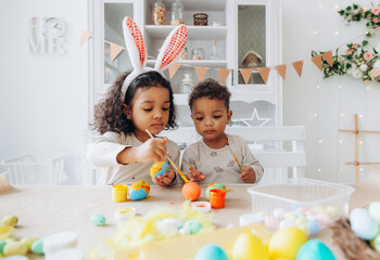 Little African American boy and girl paint Easter eggs at home. black children are preparing for Easter.