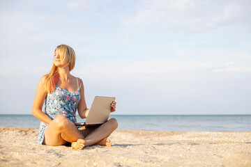 Beautiful woman with laptop computer on the beach. Working remotely on seashore. Online shopping, freelance concept - obrazy, fototapety, plakaty