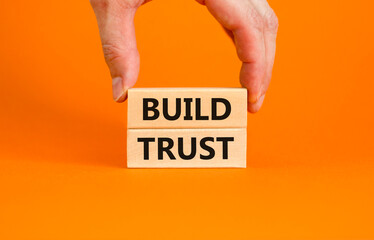 Build trust symbol. Concept words Build trust on wooden blocks on a beautiful orange table orange background. Businessman hand. Business and build trust concept, copy space.