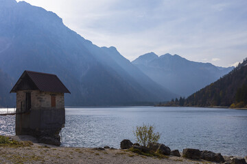 View to Julian Alps mountains above Predil lake in Italy with small lake house in a sandy coastline...