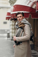  Young man wearing coat walking in the street. Young bearded guy with modern hairstyle in urban background