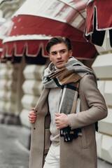  Young man wearing coat walking in the street. Young bearded guy with modern hairstyle in urban background