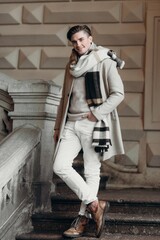  Young man wearing coat walking in the street. Young bearded guy with modern hairstyle in urban background