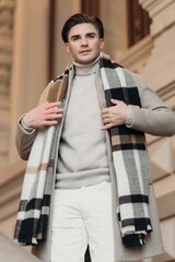  Young man wearing coat walking in the street. Young bearded guy with modern hairstyle in urban background