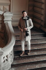  Young man wearing coat walking in the street. Young bearded guy with modern hairstyle in urban background