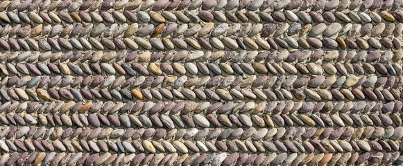 Wall of stones of various colors positioned in an orderly way in a herringbone pattern.