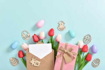 A bouquet of tulips with a postcard, a gift and wooden Easter eggs on a blue background.