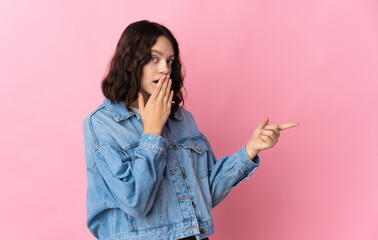 Teenager Ukrainian girl isolated on pink background with surprise expression while pointing side