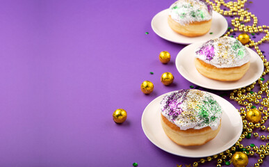 Mardi Gras King Cake sufganiyot donuts, masquerade festival carnival gold beads and golden, green, purple confetti on purple background.