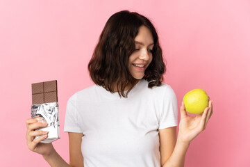 Teenager Ukrainian girl isolated on pink background taking a chocolate tablet in one hand and an...