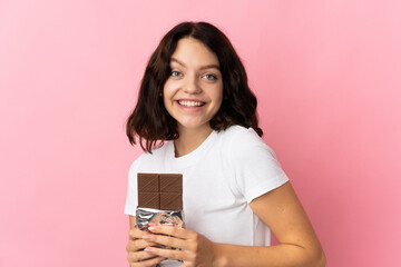 Teenager Ukrainian girl isolated on pink background taking a chocolate tablet and happy