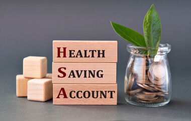 HEALTH SAVING ACCOUNT - words on wooden blocks with a jar of coins on a gray background