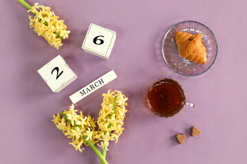 Calendar for March 26: cubes with the number 26, the name of the month of March in English, yellow hyacinths, a cup of tea, homemade cakes on a pastel background, top view