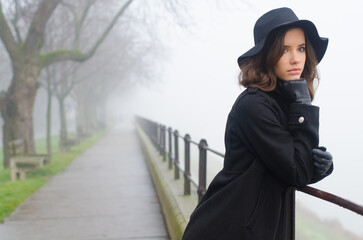 Beautiful woman in black clothes standing outdoors on a misty winter day