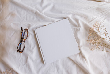 White book mockup with some glasses and dry sheets on the bed.