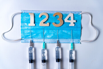 Fourth covid vaccine shot and jab concept with face mask. Four syringes are seen on table as a...