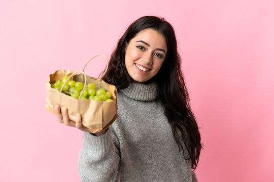 Young caucasian woman holding a grapes isolated on blue background with happy expression