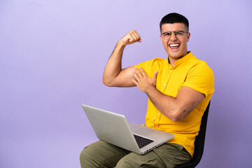 Young man sitting on a chair with laptop doing strong gesture