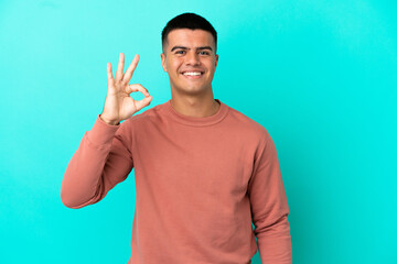 Naklejka premium Young handsome man over isolated blue background showing ok sign with fingers