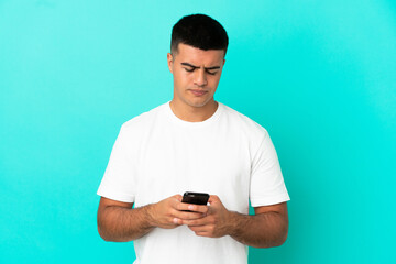Young handsome man over isolated blue background using mobile phone