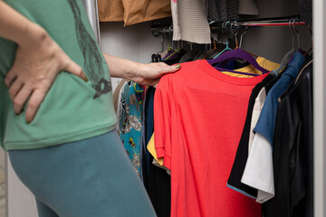 woman chooses red t-shirt in wardrobe at home