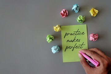 Top view image of hand holding pen, crumpled paper and green paper with text PRACTICE MAKES PERFECT.