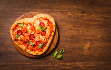 Pizza heart shaped on wooden background with copy space. Delicious Italian pizza delivery concept menu.