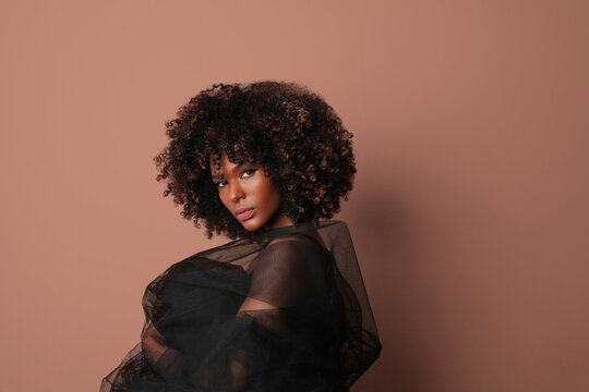 African American woman with curly hair posing over beige background.