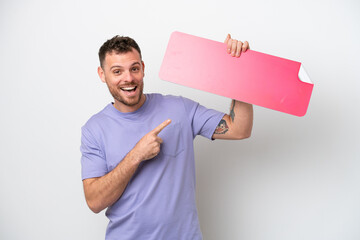 Young Brazilian man isolated on white background holding an empty placard and pointing it