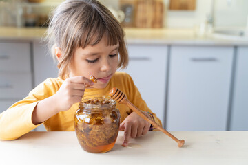 Child girl eating golden honeycomb and beeswax in a jar of honey on the table. Fresh organic honey...