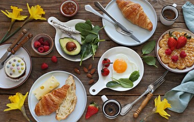Breakfast food table. Festive brunch set, meal variety with  fried egg, croissant sandwich, cheese, avocado and desserts. Overhead view