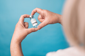 Naklejka premium Woman hands hold vial of Covid - 19 vaccine on blue background