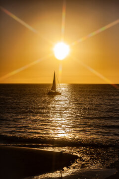Silhouette eines Segelboots im Sonnenuntergang fotografiert mit einem Sternfilter, Sonnenstrahlen