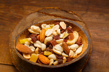 A mixture of dried fruits and nuts in a coconut shell plate on a wooden table.