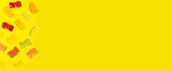 Multicolored flying gummy bears on yellow background, flat lay. Banner