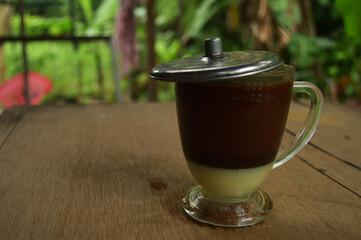 Photo of a coffee dish in a clear glass. outdoor wooden background.