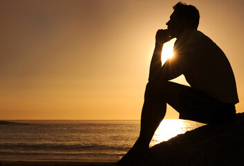 Searching for lifes answers. Silhouette of a thoughtful man sitting by the ocean - copyspace.