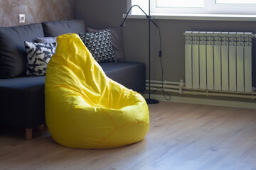 Yellow upholstered bag chair in the interior of a gray dark modern room of a teenage boy or a...