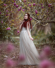 Fototapeta premium Elf girl surrounded by branches of blooming pink magnolia