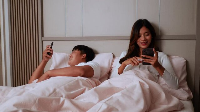 Slow motion shot, Young Couple lying on bed in bedroom, They are enjoy with social media networks addicts surf the internet on mobile phones ignoring each other, family addicted smartphone concept