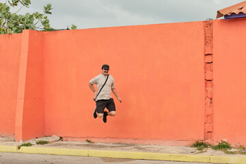 Mature Asian man in casual clothes jumping on background of bright orange wall.