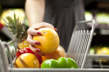Reaching for some vitamin C. A womanamp039s hand placing an orange into a shopping cart.