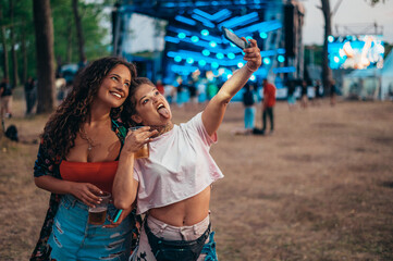 Two beautiful friends taking a selfie with a smartphone on a music festival