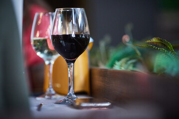 Romantic room with wine glasses in luxury interior. Two glasses of wine with red and white wine are on the table in the room with flowers.